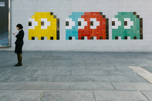 A person looking at their phone stands next to four differently coloured space invader characters of a wall