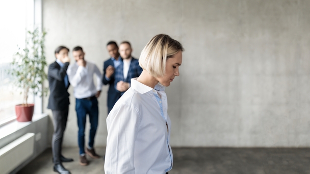 Male Colleagues Whispering Behind Back Of Unhappy Business Lady