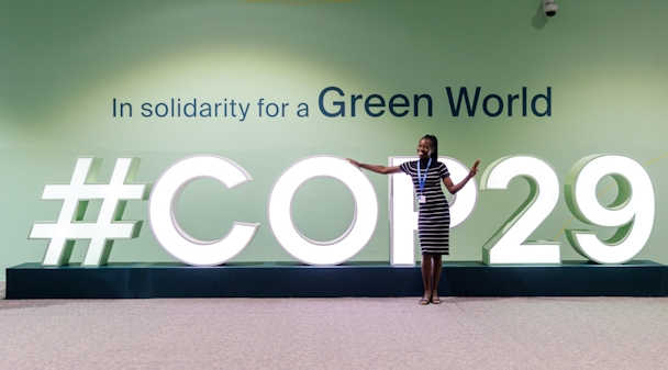 A delegate stands in front of a logo for COP29