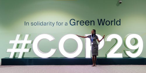 A delegate stands in front of a logo for COP29