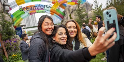 Three people take a selfie in front of an inflatable 'Dreamforce' sign 