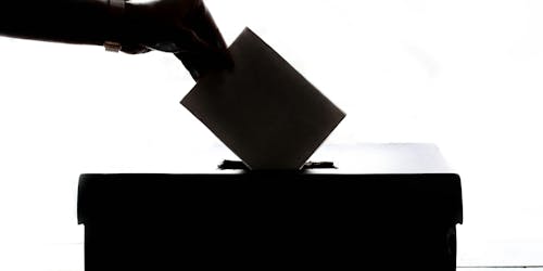 A hand places a voting paper into a ballot box