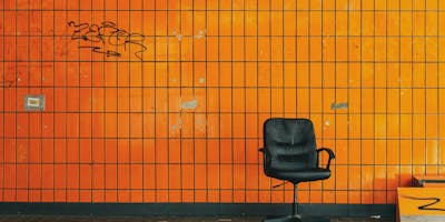 A desk chair on a street, in front of an orange wall