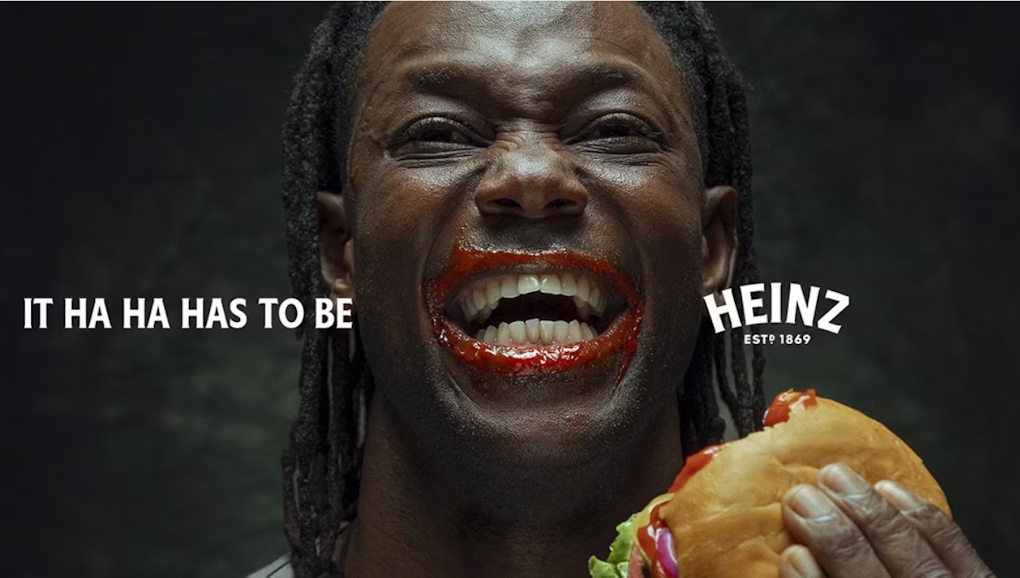 A black man with ketchup on his lips holding a burger with the slogan: It Has to be Heinz'