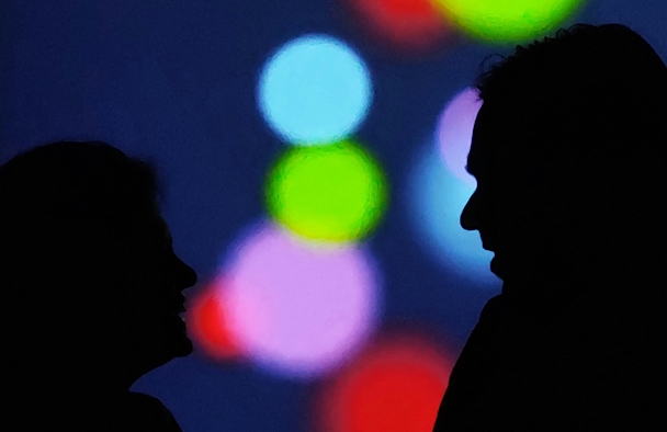 Two people in silhouette speak against a multicolored background