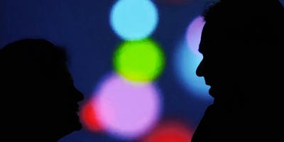 Two people in silhouette speak against a multicolored background