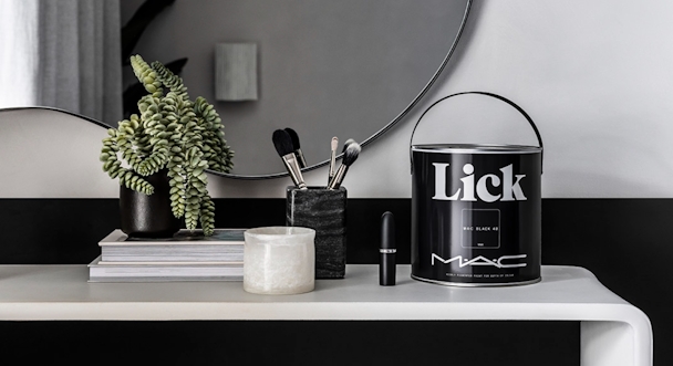 A tin of Mac x Lick paint on a desk with a plant