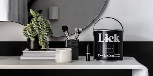 A tin of Mac x Lick paint on a desk with a plant