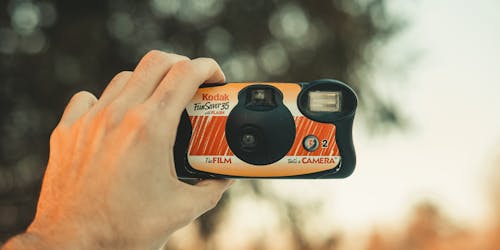 A Kodak disposable camera, held aloft as if about to take an analog selfie