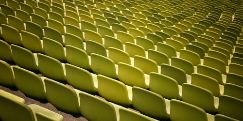 The backs of green empty rows of chairs at a stadium