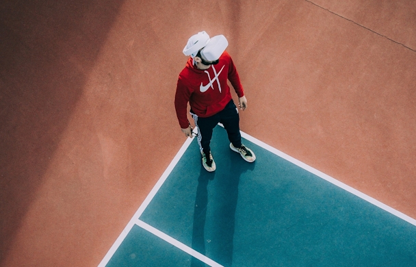 A man wearing a VR headset stands outside on a tennis court