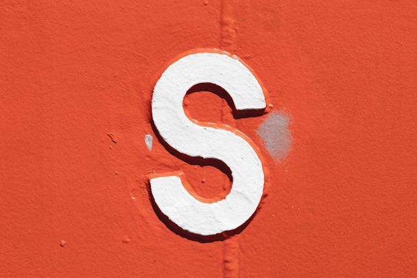 A white letter 's' with a black outline painted onto an orange wall