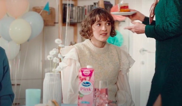 A woman sits at a table at a party with a carton of juice in front of her