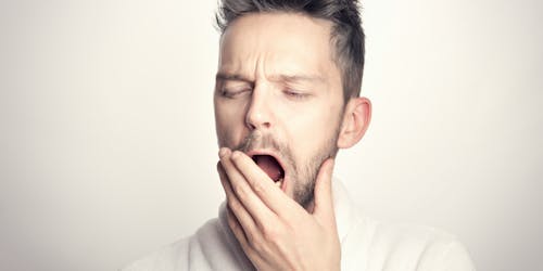 A man in a light-colored shirt raises his hand to his mouth as he yawns