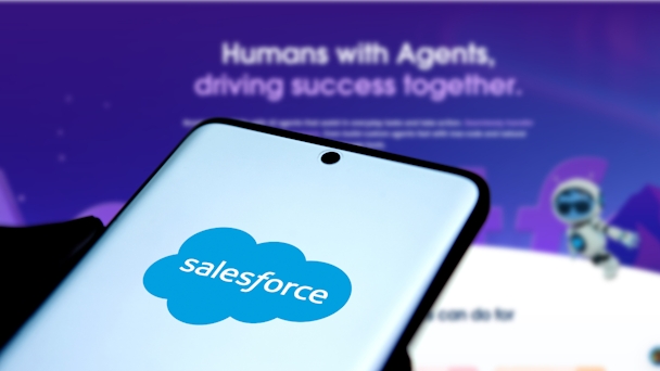 Salesforce logo on mobile phone screen in front of Agentforce landing page in the background