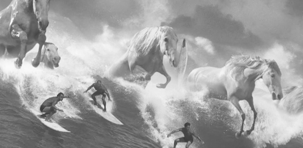 Crashing waves turn into white horses as surfers ride them