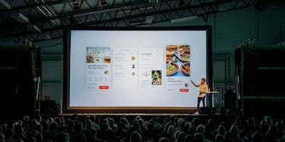 A speaker at a conference points to a screen